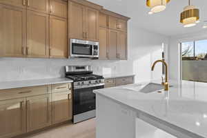 Kitchen featuring appliances with stainless steel finishes, decorative light fixtures, light stone counters, tasteful backsplash, and recessed lighting