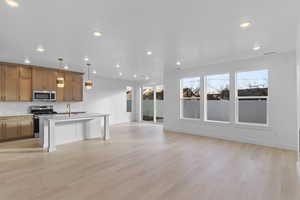 Kitchen featuring a kitchen breakfast bar, stainless steel appliances, a kitchen island with sink, open floor plan, and decorative light fixtures