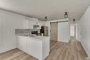 Kitchen featuring light countertops, backsplash, a barn door, stainless steel appliances, and a peninsula