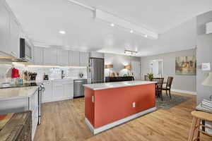 Kitchen featuring appliances with stainless steel finishes, a center island, decorative backsplash, light wood-style floors, and recessed lighting