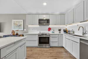 Kitchen featuring stainless steel appliances, light stone countertops, light wood-style floors, decorative backsplash, and white cabinets