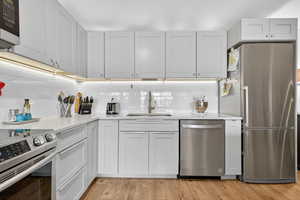 Kitchen with appliances with stainless steel finishes, light stone countertops, light wood-type flooring, and white cabinetry