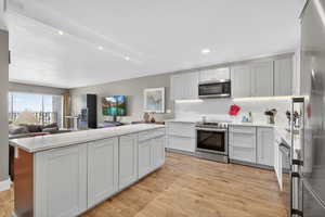Kitchen featuring backsplash, appliances with stainless steel finishes, open floor plan, light wood-type flooring, and recessed lighting