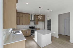 Kitchen with decorative backsplash, light stone counters, stainless steel gas stove, recessed lighting, and wall chimney range hood