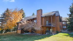 Back of property featuring a yard, a chimney, a patio area, a balcony, and a shingled roof