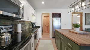Kitchen with green cabinetry, wooden counters, appliances with stainless steel finishes, white cabinetry, and backsplash