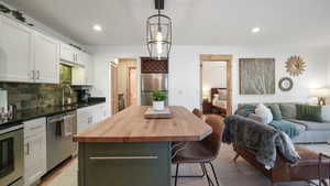 Kitchen with white cabinets, wooden counters, open floor plan, a kitchen breakfast bar, and decorative backsplash