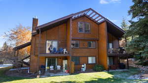 Back of property featuring a chimney, a lawn, a patio, and a balcony