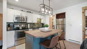 Kitchen featuring white cabinetry, stainless steel appliances, a kitchen breakfast bar, and baseboard heating
