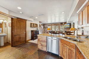 Kitchen with dishwasher, light stone countertops, brown cabinetry, a peninsula, and open floor plan