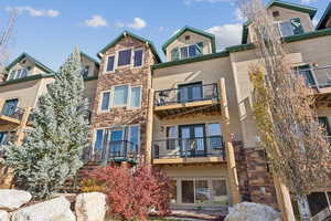 Back of property with stone siding, a balcony, and a gambrel roof