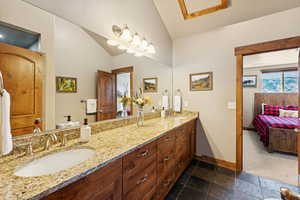 Full bath featuring double vanity, ensuite bathroom, stone tile flooring, and lofted ceiling
