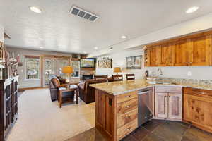 Kitchen with a stone fireplace, a peninsula, brown cabinetry, light stone countertops, and recessed lighting