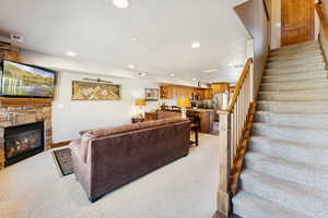 Living room with stairs, recessed lighting, light colored carpet, and a stone fireplace