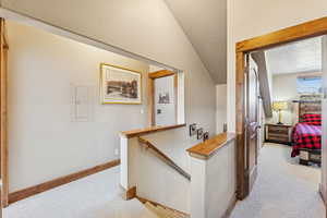 Hall with light colored carpet, a textured ceiling, an upstairs landing, electric panel, and lofted ceiling