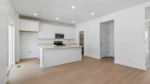 Kitchen featuring white cabinets, a center island with sink, light wood finished floors, stainless steel appliances, and recessed lighting