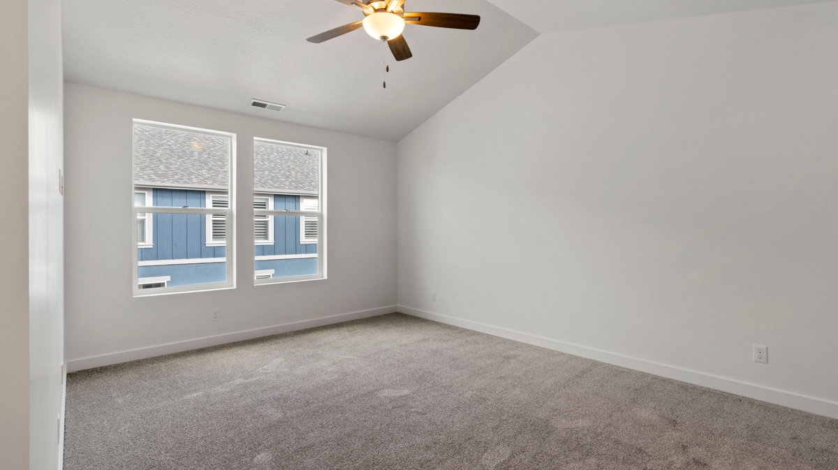 Spare room featuring light colored carpet, vaulted ceiling, and a ceiling fan