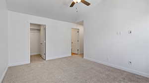 Unfurnished bedroom featuring a spacious closet, light carpet, vaulted ceiling, and ceiling fan
