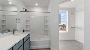 Bathroom featuring vanity, shower / bath combination, a walk in closet, recessed lighting, and light colored carpet