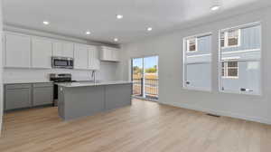 Kitchen with gray cabinets, stainless steel appliances, white cabinetry, a kitchen island with sink, and light wood finished floors