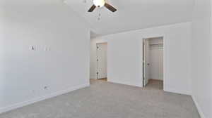 Unfurnished bedroom featuring light colored carpet, a spacious closet, lofted ceiling, and a ceiling fan