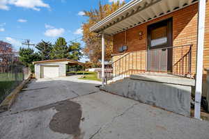 Doorway to property with brick siding, a detached garage, concrete driveway, and a carport