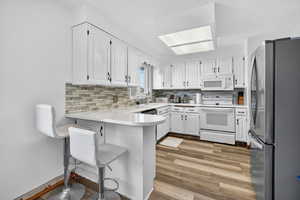 Kitchen with appliances with stainless steel finishes, white cabinetry, a peninsula, light countertops, and a breakfast bar area