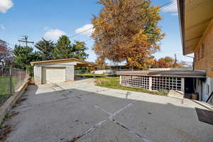 View of patio with an outbuilding, concrete driveway, a garage, and a carport