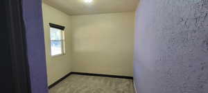 Empty room with a textured wall, a textured ceiling, and light colored carpet