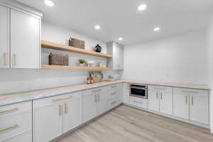 Kitchen featuring recessed lighting, open shelves, light stone countertops, light wood finished floors, and stainless steel oven