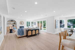 Living area with light wood-style floors, built in shelves, recessed lighting, a glass covered fireplace, and a textured ceiling
