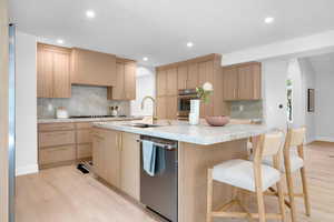 Kitchen with arched walkways, light wood-type flooring, appliances with stainless steel finishes, tasteful backsplash, and light stone countertops