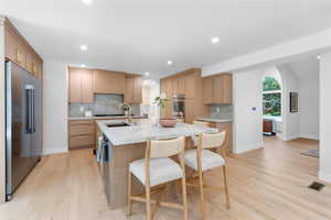 Kitchen featuring arched walkways, appliances with stainless steel finishes, light wood-type flooring, decorative backsplash, and recessed lighting