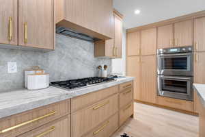 Kitchen featuring stainless steel appliances, light wood-style flooring, light brown cabinetry, custom exhaust hood, and decorative backsplash