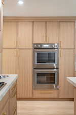 Kitchen with stainless steel double oven, light wood finished floors, light brown cabinets, modern cabinets, and recessed lighting