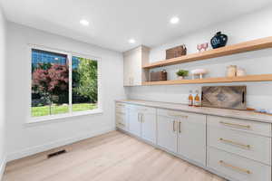 Bar featuring open shelves, light wood-style floors, light stone counters, and recessed lighting