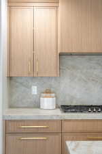 Kitchen featuring stainless steel gas stovetop, tasteful backsplash, light brown cabinetry, range hood, and light stone counters