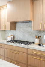 Kitchen with extractor fan, light brown cabinetry, backsplash, light stone countertops, and stainless steel gas stovetop