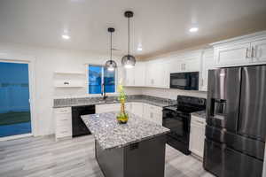 Kitchen featuring black appliances, white cabinetry, light stone countertops, a center island, and recessed lighting