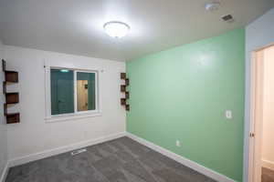 Unfurnished room featuring dark colored carpet and a smoke detector