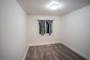 Unfurnished room featuring dark colored carpet and baseboards