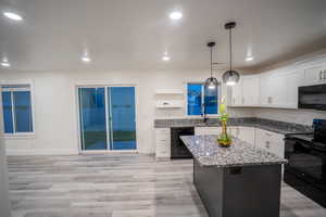 Kitchen with black appliances, white cabinets, dark stone counters, pendant lighting, and a kitchen island