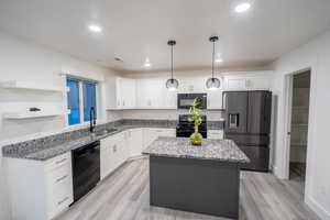 Kitchen with a center island, black appliances, white cabinets, dark stone countertops, and recessed lighting