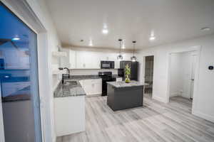 Kitchen featuring white cabinetry, dark stone counters, black appliances, decorative light fixtures, and a kitchen island