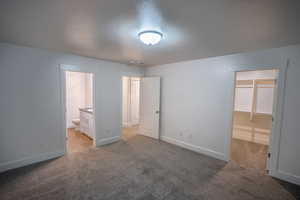 Unfurnished bedroom featuring light carpet, a walk in closet, and ensuite bathroom