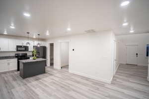 Kitchen with white cabinets, pendant lighting, black appliances, recessed lighting, and light wood-type flooring