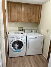 Laundry area featuring cabinet space, light wood finished floors, washer and dryer, and a textured ceiling