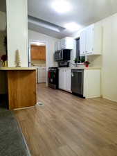 Kitchen with light wood-style flooring, appliances with stainless steel finishes, light countertops, a textured ceiling, and white cabinetry