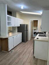 Kitchen with open shelves, white cabinets, light wood-type flooring, light countertops, and washer / clothes dryer