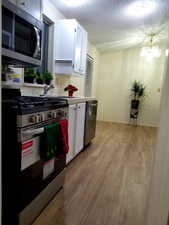 Kitchen with appliances with stainless steel finishes, white cabinets, light wood finished floors, a textured ceiling, and light countertops